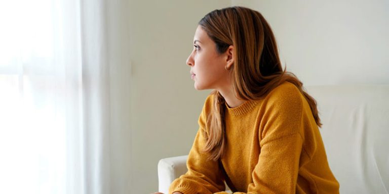 adolescente sentada em um sofá com expressão de preocupação e tensão